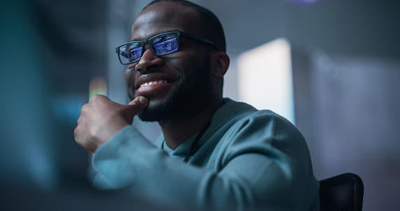 Close Up Of Black Male Developer Smiling Happily After Successfully Typing on Computer a Functioning Software Code. Professional Programmer Creating Mobile App, Screen Display Reflected on his Glasses