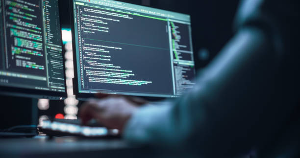 istock Close Up on Black Male Hands Typing on a Desktop Computer Keyboard In Dark Network Security Office. Professional Programmer Writing Code Displayed on Two Monitor Screens. High Tech Developing Concept. 1518853764