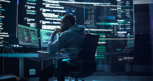 istock Portrait of a Black Man Working on Computer, Typing Lines of Code that Appear on Big Screens Surrounding him in Monitoring Room. Male Programmer Creating Innovative Software Using AI Data and System 1518855320