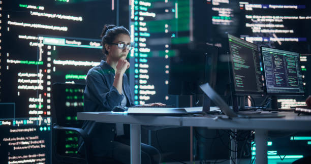 istock Focused Woman Working on a Computer, Typing Lines of Code that Appear on Big Screens Surrounding her in a Monitoring Room. Female Programmer Creating Innovative Software Using AI Data and System 1518856907