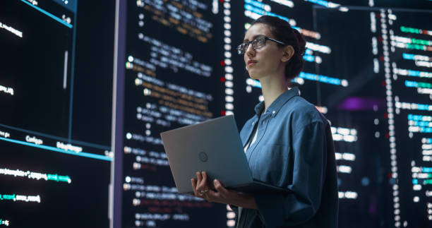 Portrait of Woman Creating a Software and Coding, Surrounded by Big Screens Displaying Lines of Programming Language Code. Female Programmer Working in a Monitoring Room. Futuristic Concept