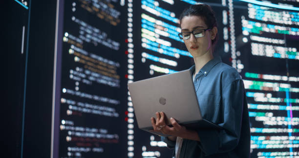 istock Portrait of Woman Creating a Software and Coding, Surrounded by Big Screens Displaying Lines of Programming Language Code. Female Programmer Working in a Monitoring Control Room. Futuristic Concept 1518864070