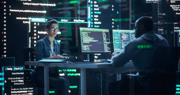 istock Diverse Young Man and Woman Working on Desktop Computers, Surrounded by Big Screens Displaying Code Lines. Professional Computer Engineers Developing Autonomous Algorithm for Generative AI. 1518865943
