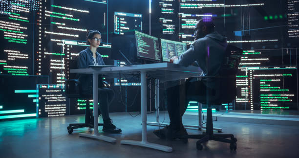 istock Diverse Young Man and Woman Working on Desktop Computers, Surrounded by Big Screens Displaying Code Lines. Professional Computer Engineers Developing Autonomous Algorithm for Generative AI 1518865983
