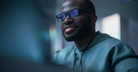 Black Male Developer Smiling Happily After Successfully Typing on Computer a Functioning Software Code. Professional Programmer Creating a Mobile App, Screen Display Reflected on his Glasses