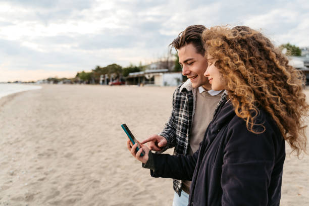 istock Young Couple Using Phone On The Beach In Greece 1518930341