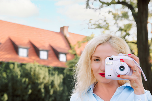 a woman on the street takes pictures on a polaroid. a warm summer day. Europe