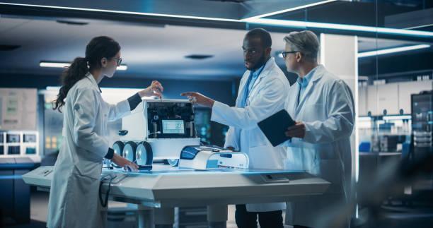 istock Diverse Team of Industrial Robotics Specialists Gathered Around Table With a Mobile Robot. Engineers In Lab Coats Discussing an Automated Robotic Delivery Machine with Artificial Intelligence 1518977090