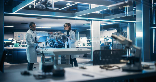 istock Young Engineers Using Tablet and Laptop Computers, Collaborate on a New Type of a Electric Turbine Engine, Using Software for Testing Equipment in Scientific Technology Laboratory 1518978177