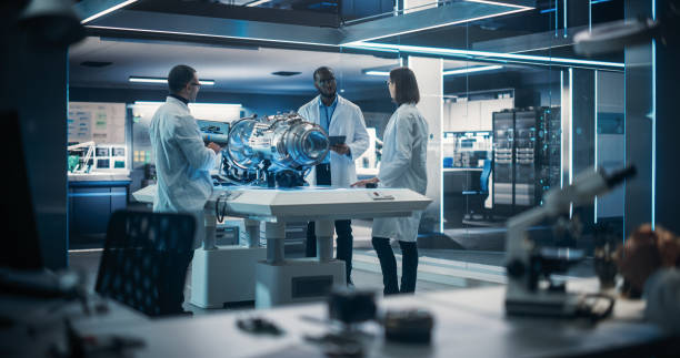 istock Smart Team of Engineers, Project Manager and Machinery Operators Collaborate on a New Type of a Electric Turbine Engine, Standing with Tablet and Laptop Computers in Scientific Technology Lab 1518979301