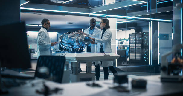 istock Smart Team of Engineers, Project Manager and Machinery Operators Collaborate on a New Type of a Electric Turbine Engine, Standing with Tablet and Laptop Computers in Scientific Technology Laboratory 1518982512