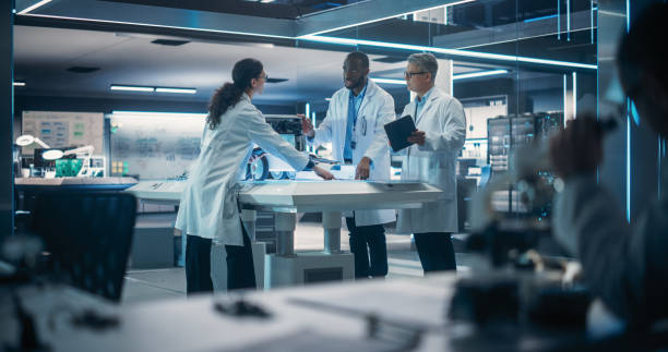 istock Industrial Robotics Specialists Working on a Mobile Robot, Using a Tablet Computer. Male Engineer In Lab Coat Discussing an Automated AI Robotic Delivery Assistant with His Young Team 1518994791