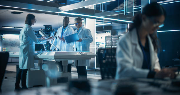 istock Proffesional Female Engineer Working on Electronic Circuit Boards. On Background Industrial Robotics Specialists in Lab Coats Working on a Mobile AI Robot in an Advanced Tech Factory Facility. 1519009042