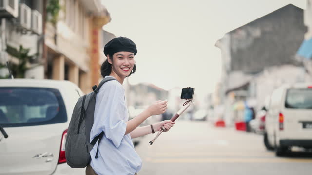 Asian Chinese young woman vlogging at Penang alley with smartphone and selfie stick