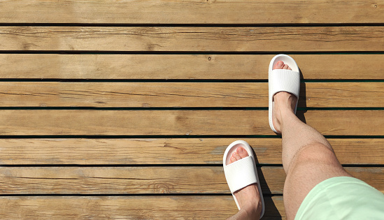 Male feet wearing white slippers on the pier
