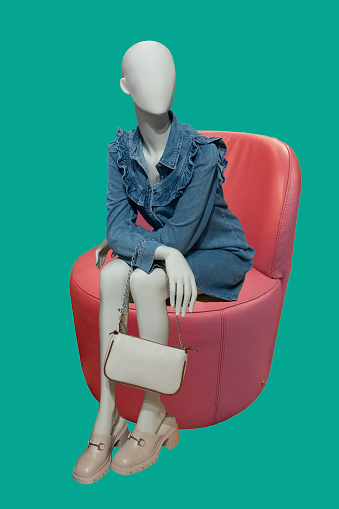 Full length image of a female display mannequin sitting on a red leather chair. Isolated on blue background