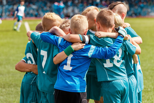 Powerful Team Unity: Children Huddling in Sports Team, Embracing Friendship and Camaraderie on a Vibrant Grass Pitch. Inspiring Youth Sports Image