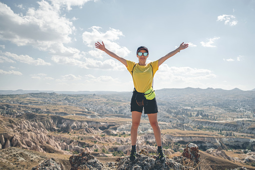 Woman tourist with backpack standing on mountain top in Cappadocia with open arms, Turkey
