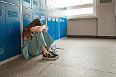 Worried teenage girl sitting on floor at school