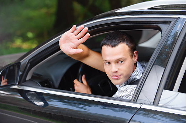 retrato de jovem homem a condução carro e cumprimentar alguém - fazendo sinal com a mão imagens e fotografias de stock