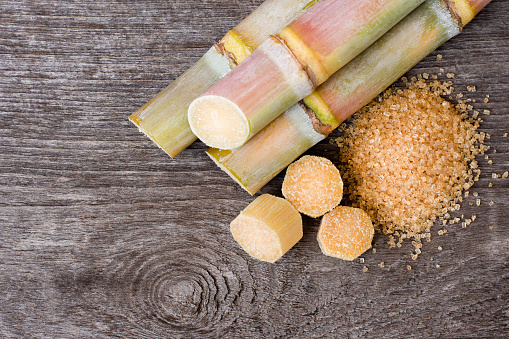 Sugar cane and brown granulated sugar on wooden table background, top view, flat lay.