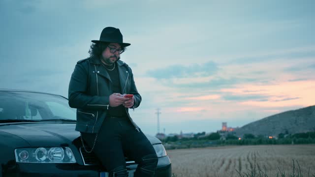Cinematic scene of a man looking his mobile phone with a car at dusk