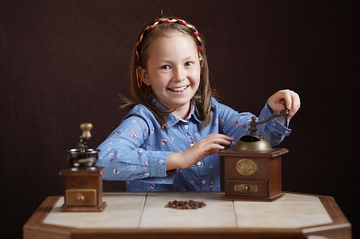 Cute girl grinding coffee beans in a retro coffee grinder. Concept: sale of fresh natural coffee