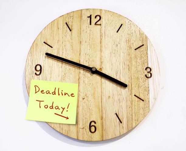 istock Wood clock on white office wall with text note DEADLINE TODAY, concept of professional time management, handling deadline stress situation when time is running out or busy tight work schedule in workplace 1519248098