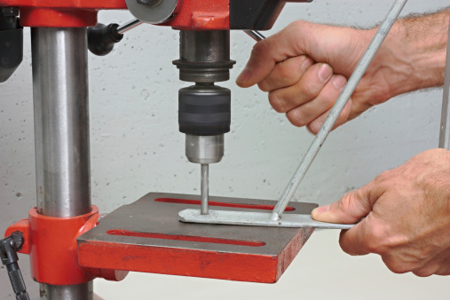 a worker drills a hole in iron bracket with a bench drill