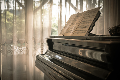 Artistic short depth of field photo of closed piano keyboard with the reflection of soft. warm yellow daylight toned bokeh lights in the background.