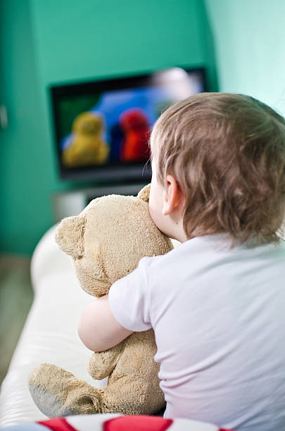istock A young boy holding onto a teddy bear while watching TV 151929426