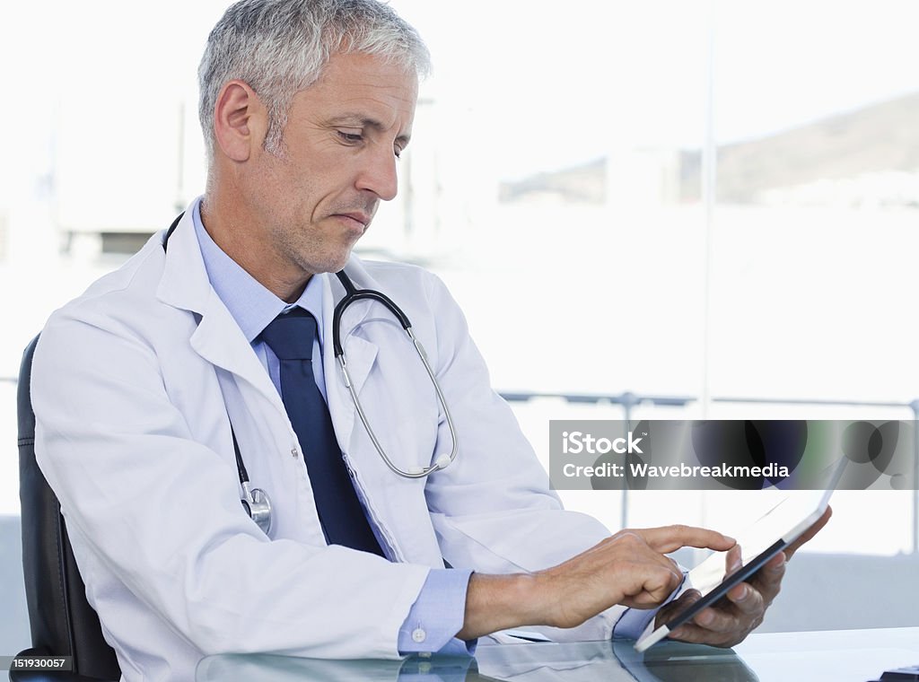 Serious doctor working with a tablet computer Serious doctor working with a tablet computer in his office Adult Stock Photo