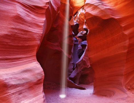 A thin ray of sunlight illuminates the sandy bottom of the canyon. Noon in Antelope Canyon.