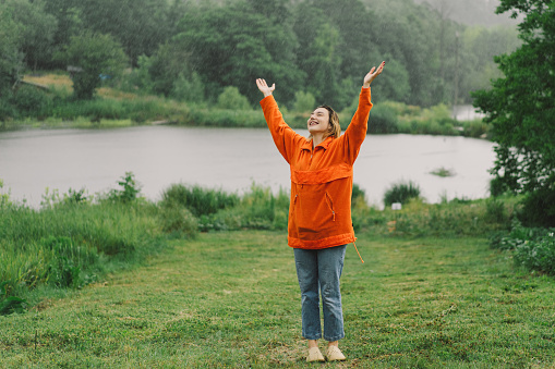 Portrait of a young girl in an orange sweater enjoying the rain on a summer day. The girl is having fun and dancing under the summer rain