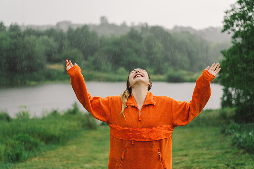Portrait of a young girl in an orange sweater enjoying the rain on a summer day. The girl is having fun and dancing under the summer rain