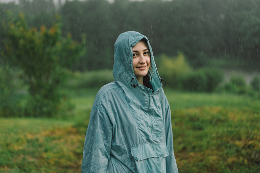 Portrait of a young girl in a blue raincoat enjoying the rain on a summer day.