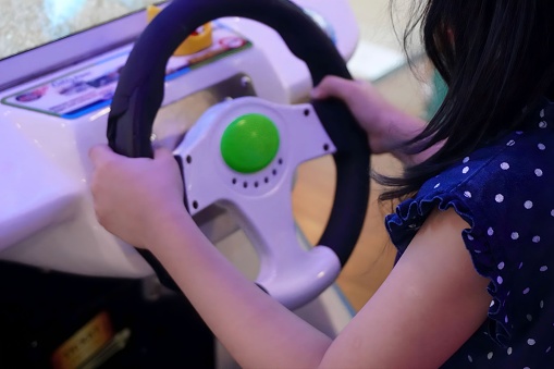 Selective image of kid playing car racing game simulator. Closeup of hand and steering wheel