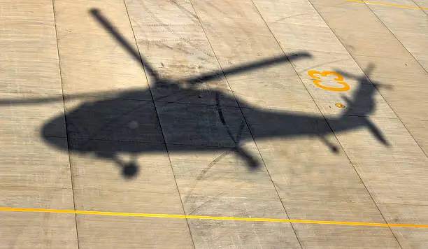 Shadow of a UH-60 Blackhawk on concrete tarmac as it takes off.