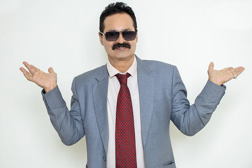 Happy mature indian businessman wearing suit and sunglasses with empty hands gesture isolated over white background. Corporate Concept.