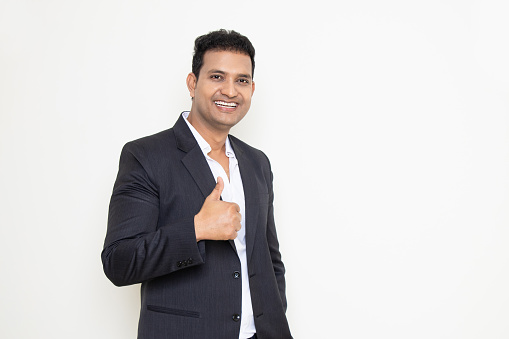 Smiling handsome young indian businessman wearing suit do thumbs up pose isolated over white background. Corporate Concept.
