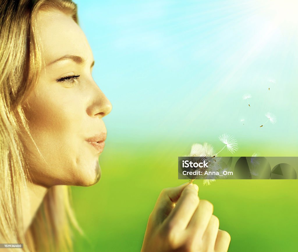 Profile of a blonde happy beautiful girl blowing a dandelion Happy beautiful woman blowing dandelion over blur background, having fun and playing outdoor, teen girl enjoying nature, summer vacation and holidays, young pretty female holding flower, wish concept Making Stock Photo