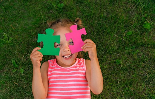 A funny girl is playing with puzzles, closing her eyes with details. Children's educational games.