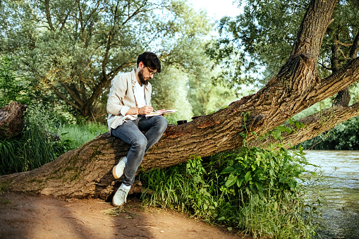 Man drawing outdoors while sitting on a tree trunk