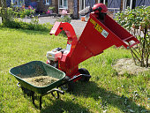 Plant shredder close to a wheelbarrow filled with mulch, in a lawn.