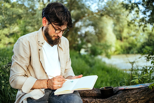 Man drawing outdoors while sitting on a tree trunk