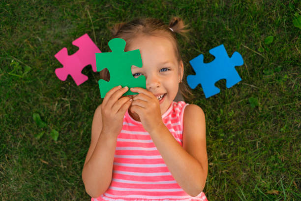 Preparation for school, development and education A cute beautiful preschool girl is lying on the grass on the lawn covering her face with puzzle pieces laughing merrily. Preparation for school, development and education preschooler caucasian one person part of stock pictures, royalty-free photos & images