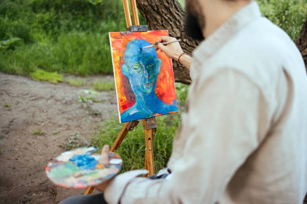 Young artist paints in nature while sitting on a tree trunk