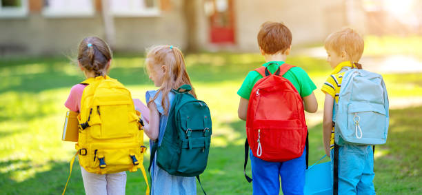 Group of children standing with backpacks near the school. stock photo