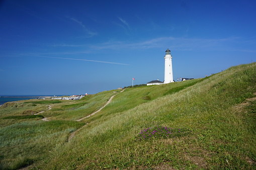 View of the lighthouse in Hirtshals on a sunny summer day. Lighthouse in Denmark on the background of blue sky and green grass. Lighthouse in Hirtshals and next to the Danish flag.