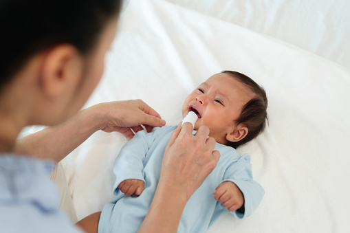 mother using finger to clean newborn baby mouth (tongue and gum) with clean gauze on a bed
